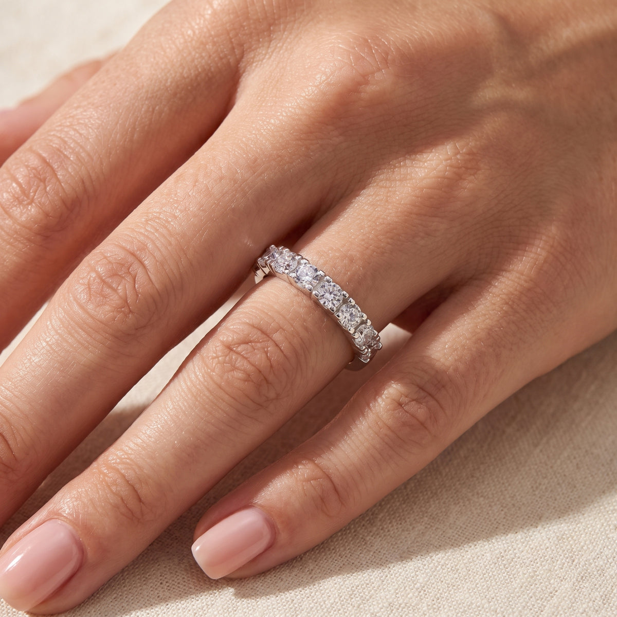 Seven-stone silver ring with round clear stones worn on a finger, viewed from above.
