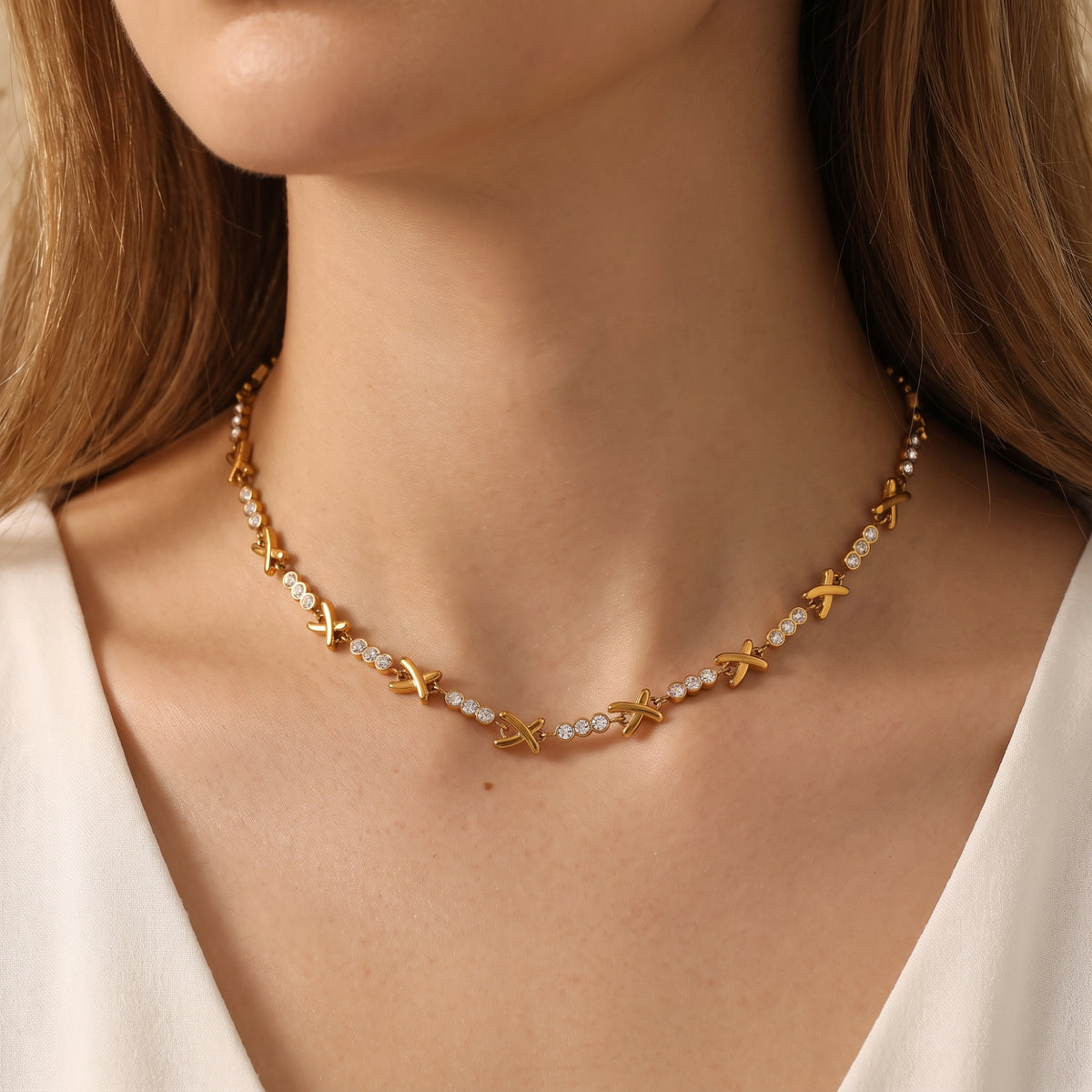 Front-facing view of the gold-tone X station necklace resting along a model's collarbone.