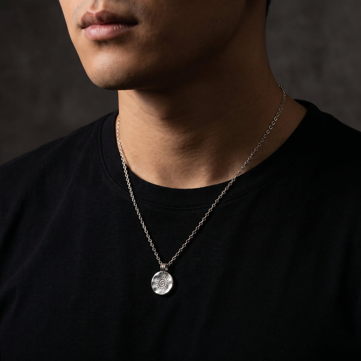 Front view of a man wearing the silver sunburst pendant necklace against a plain black T-shirt.