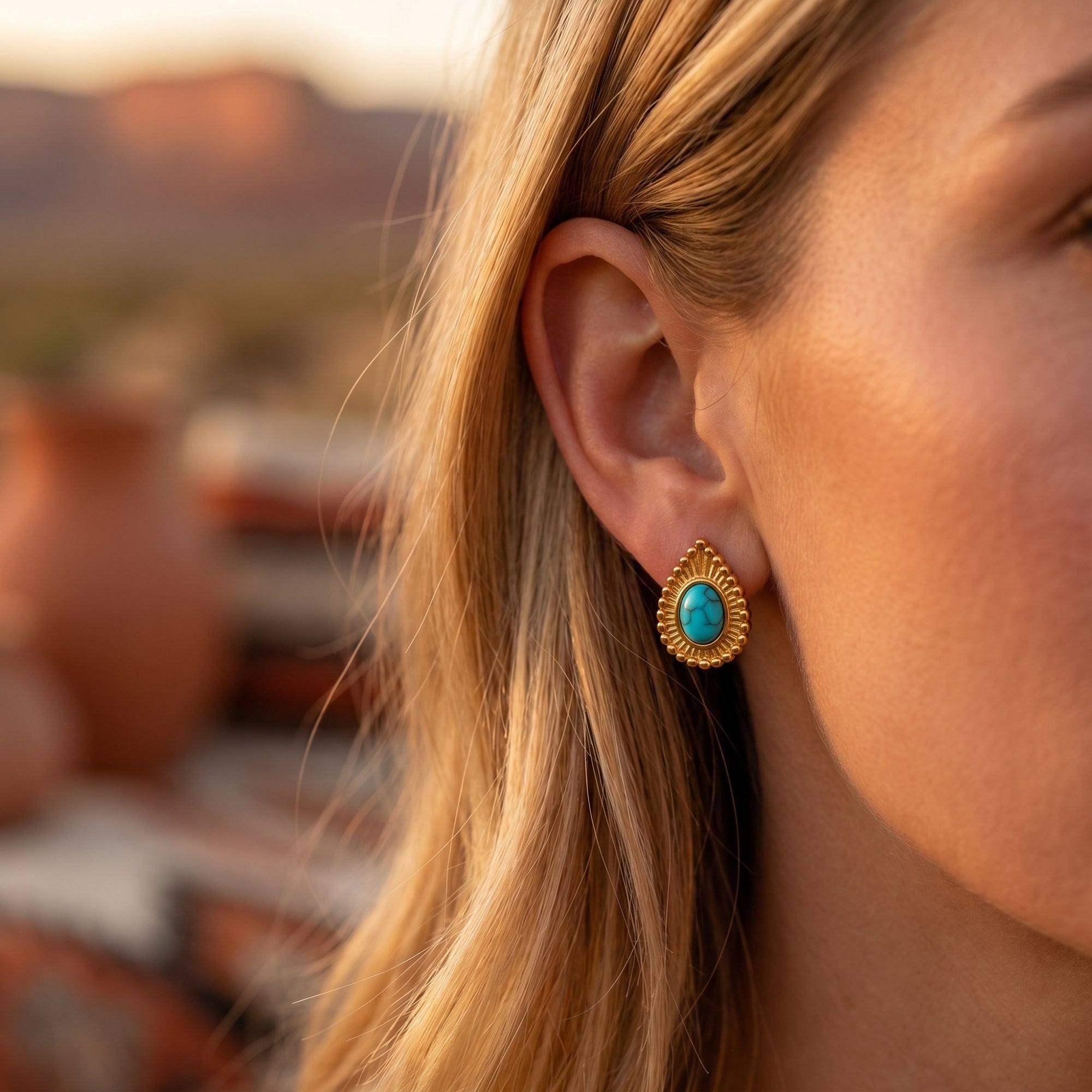 Side profile of a model wearing a turquoise-hued oval cabochon earring with a golden-beaded border.