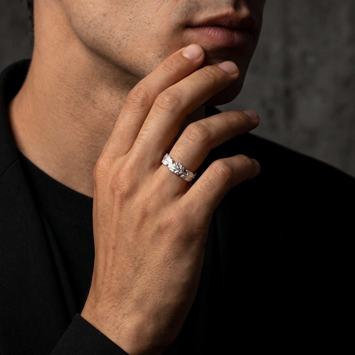 Silver oak leaf ring worn on a man's hand near his chin with a black shirt visible.