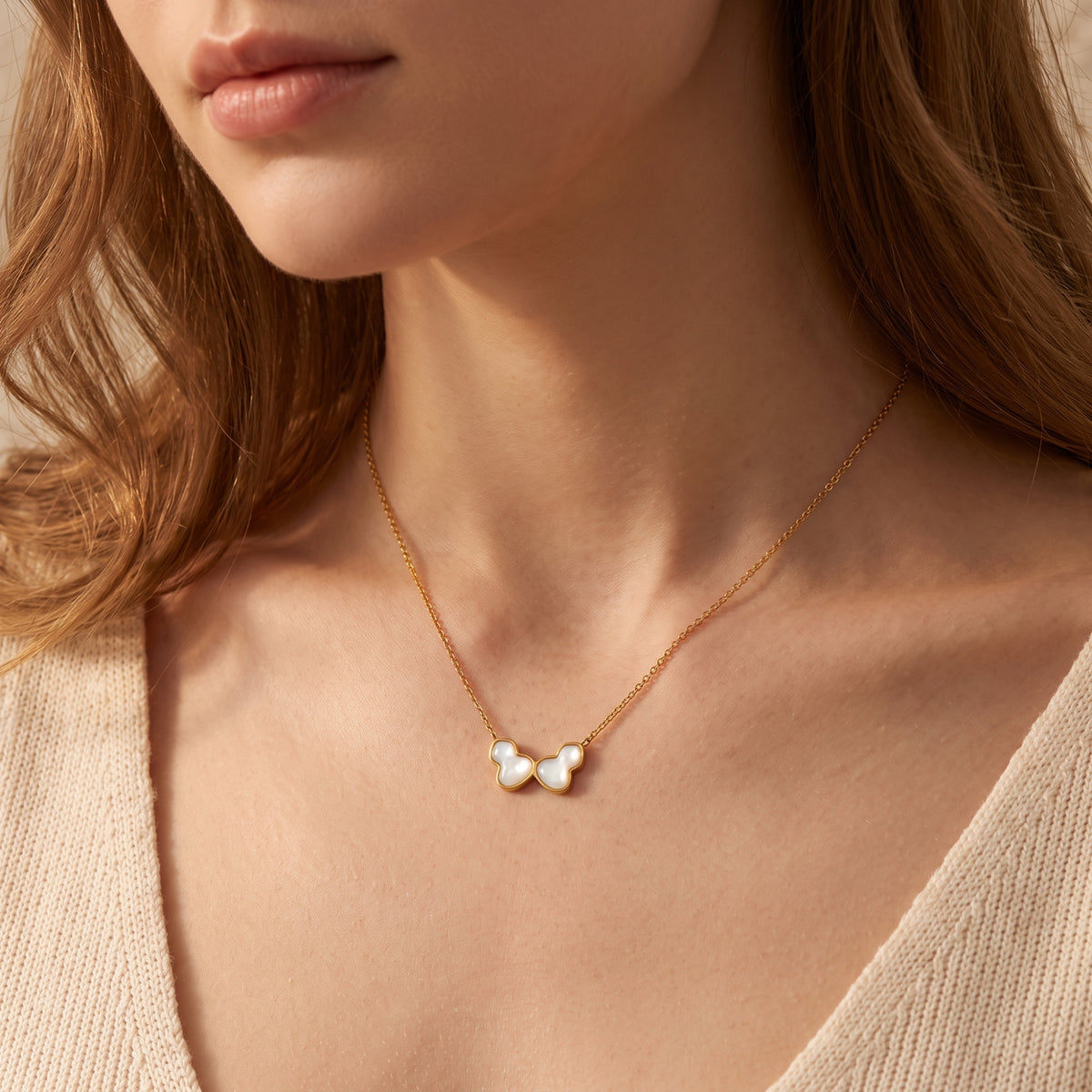 Model wearing a gold-tone butterfly necklace with white iridescent inlays and a beige ribbed knit top.