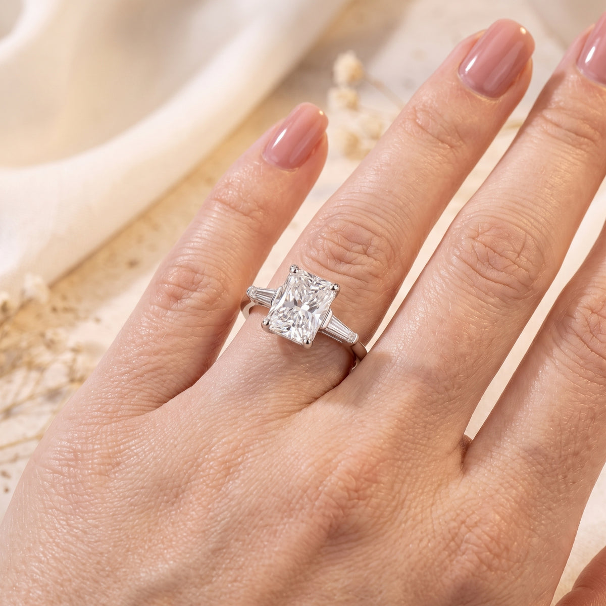Close-up of the silver radiant-cut ring on a finger, displaying the side tapered baguette stones clearly.