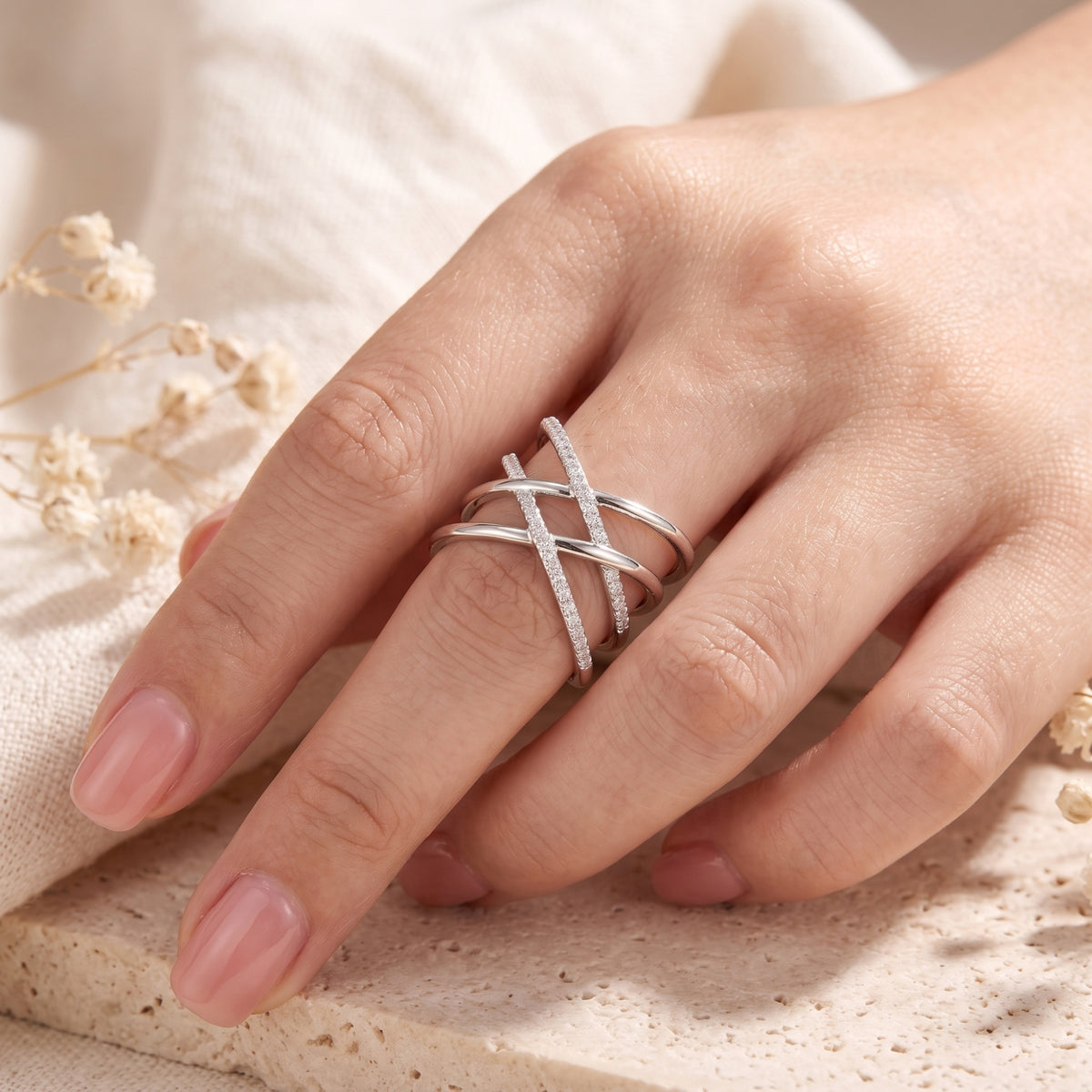 Hand resting on a stone surface while wearing a silver multi-band crossover ring with pavé stone accents.