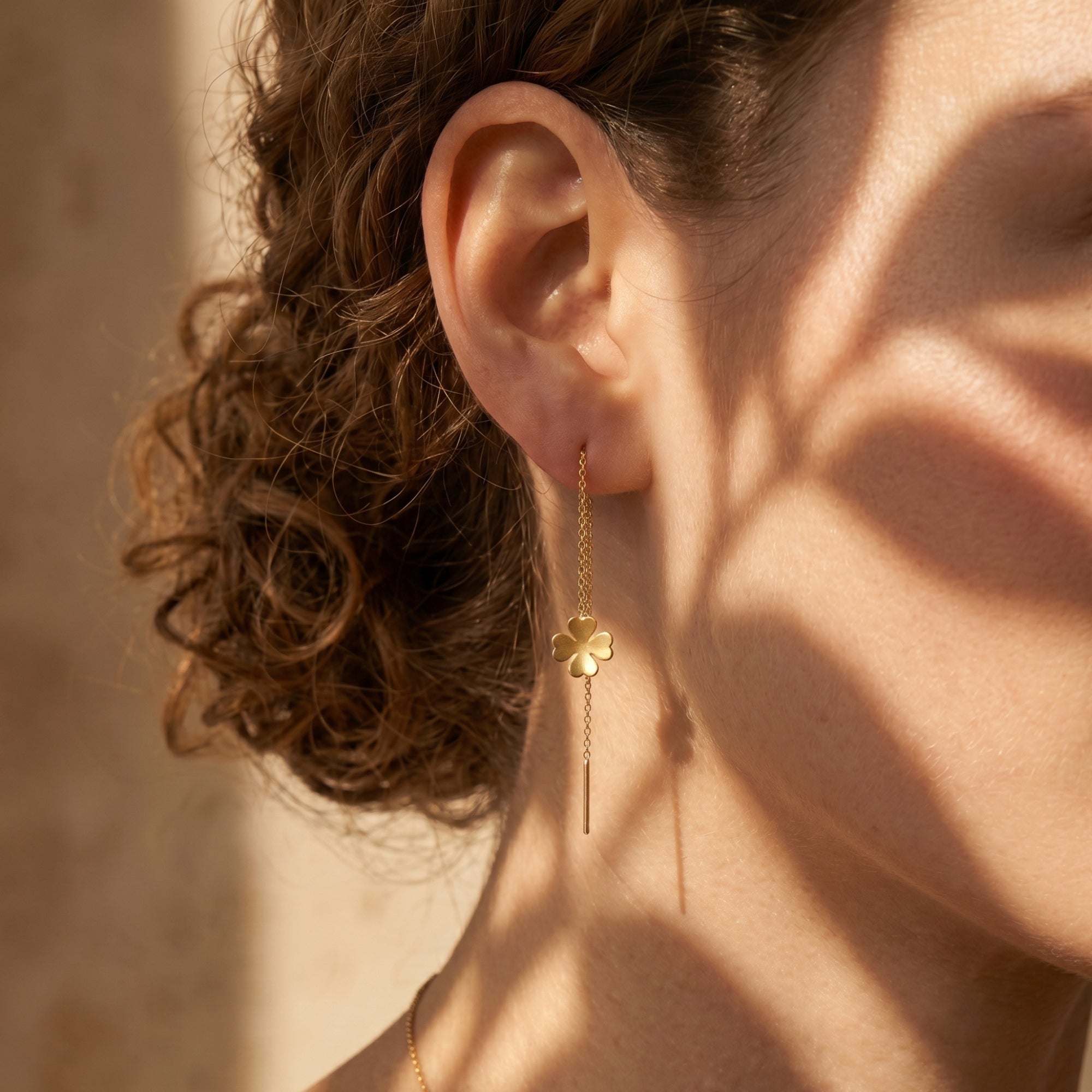 A model wearing an 18K gold finish clover threader earring with artistic leaf shadows on her face.