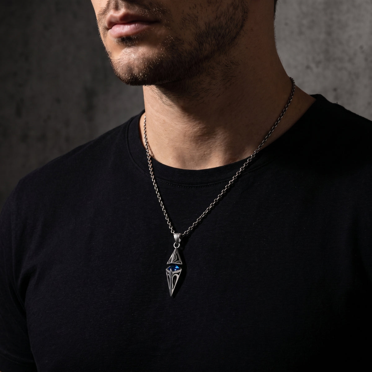 Man wearing the silver pendant necklace with a blue center stone over a plain black shirt.