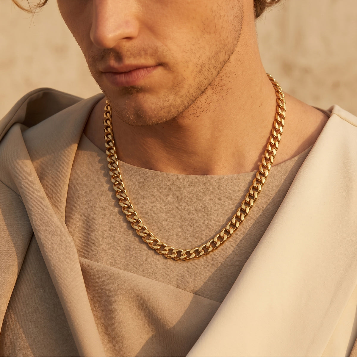 Gold-tone Cuban link chain worn around a man's neck over beige draped clothing.