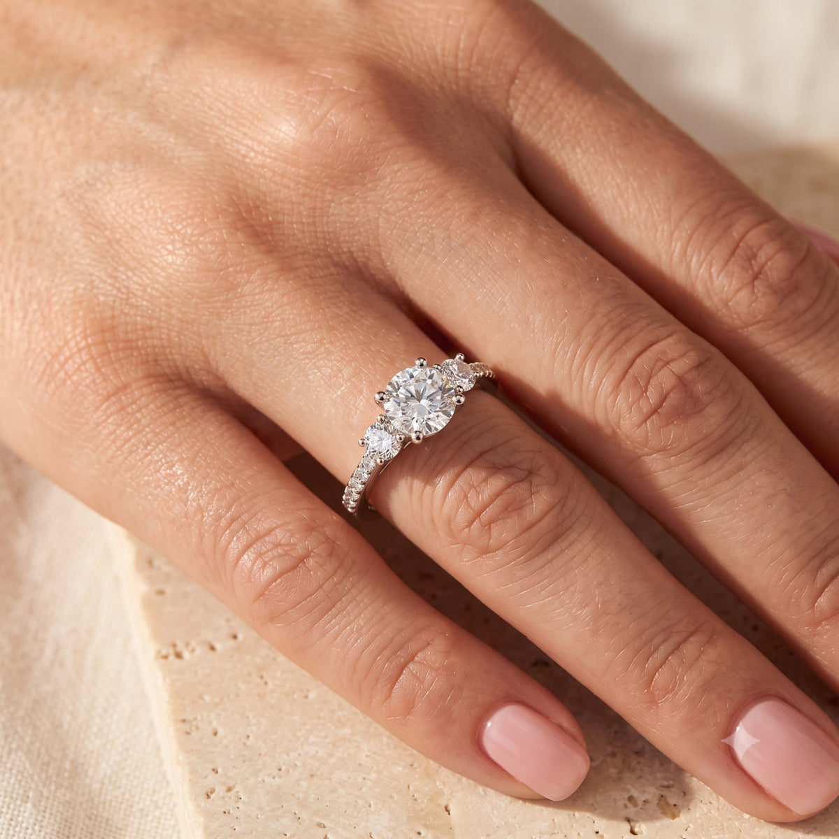 Adalicia sterling silver three-stone ring with round-cut simulated diamonds shown on a finger.