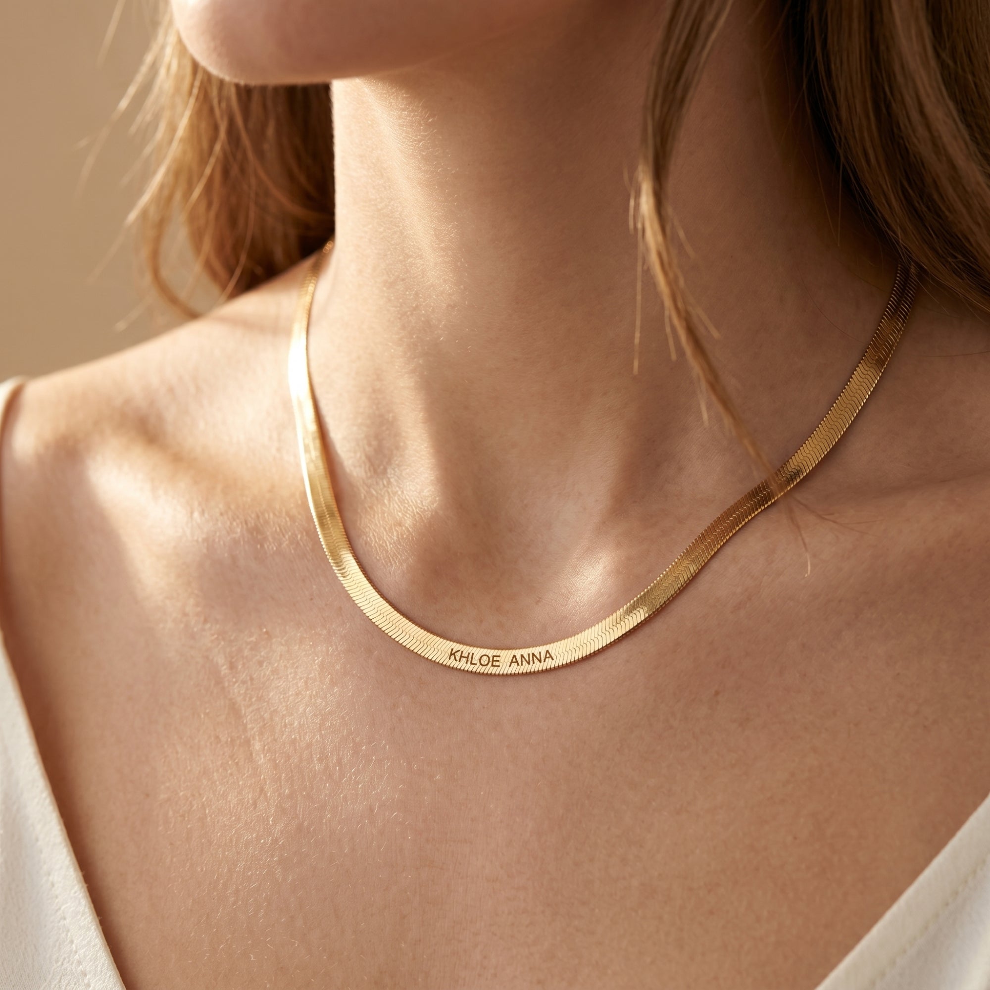 Close-up of 18K gold finish custom name herringbone necklace on a model's neck.