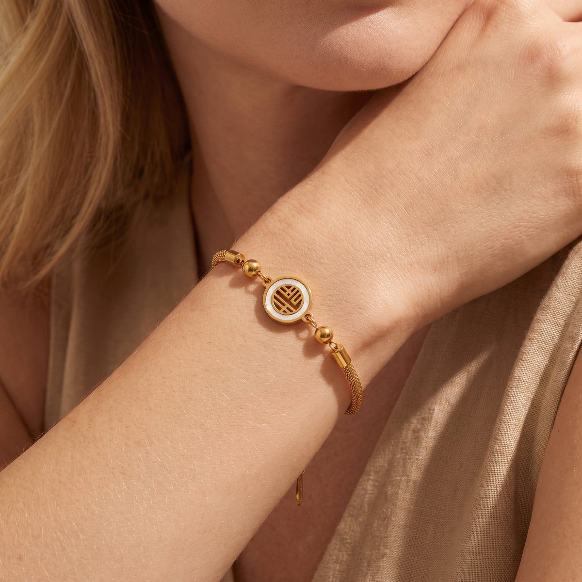 Close-up of a model wearing the gold-tone heritage medallion bracelet with hand raised to chin.
