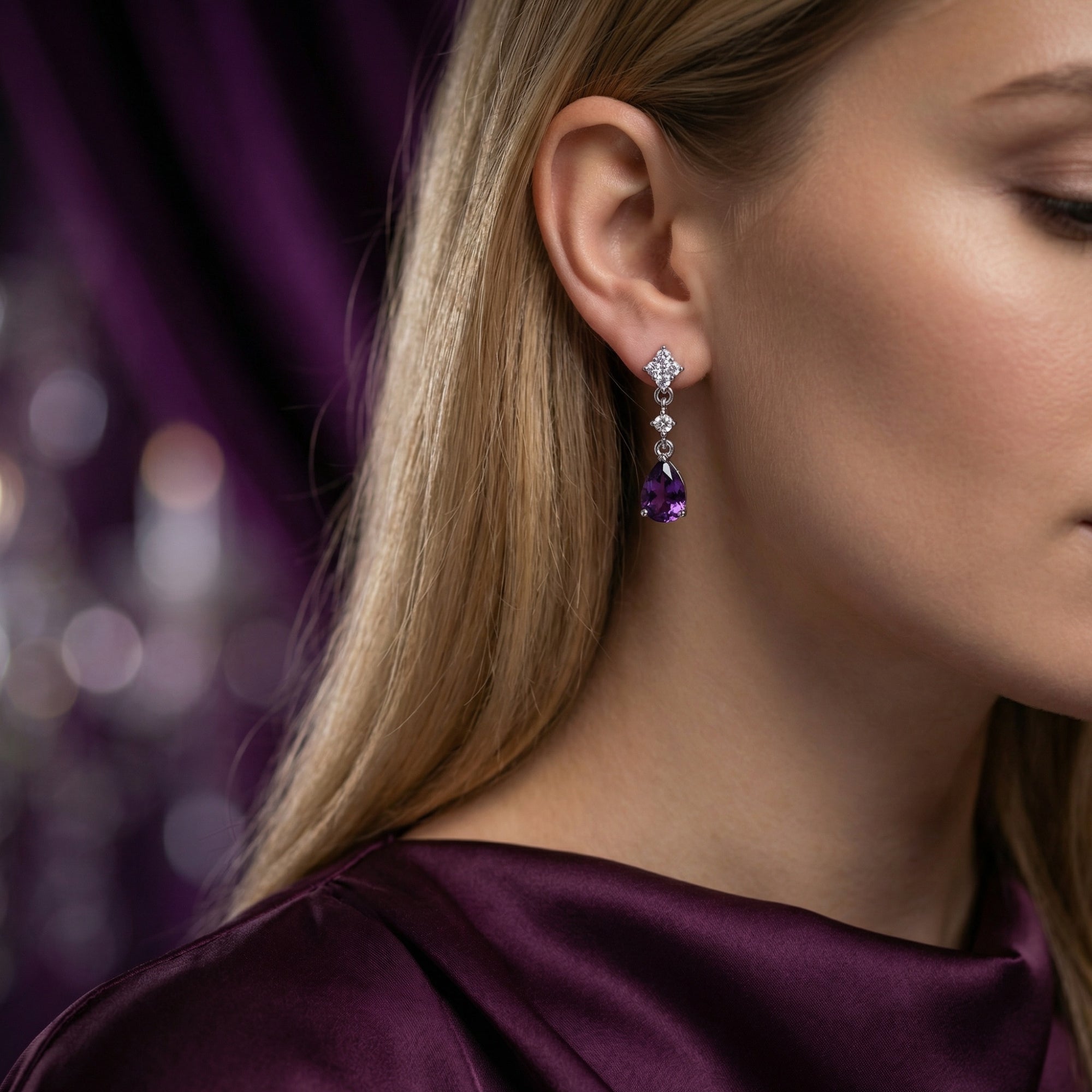 Profile view of a woman wearing a sterling silver drop earring with a faceted pear cut amethyst.