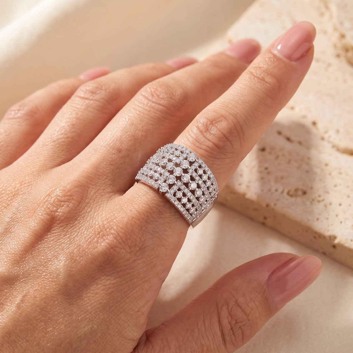 Wide silver lattice ring with clear stones, shown worn on a finger from an angled view.