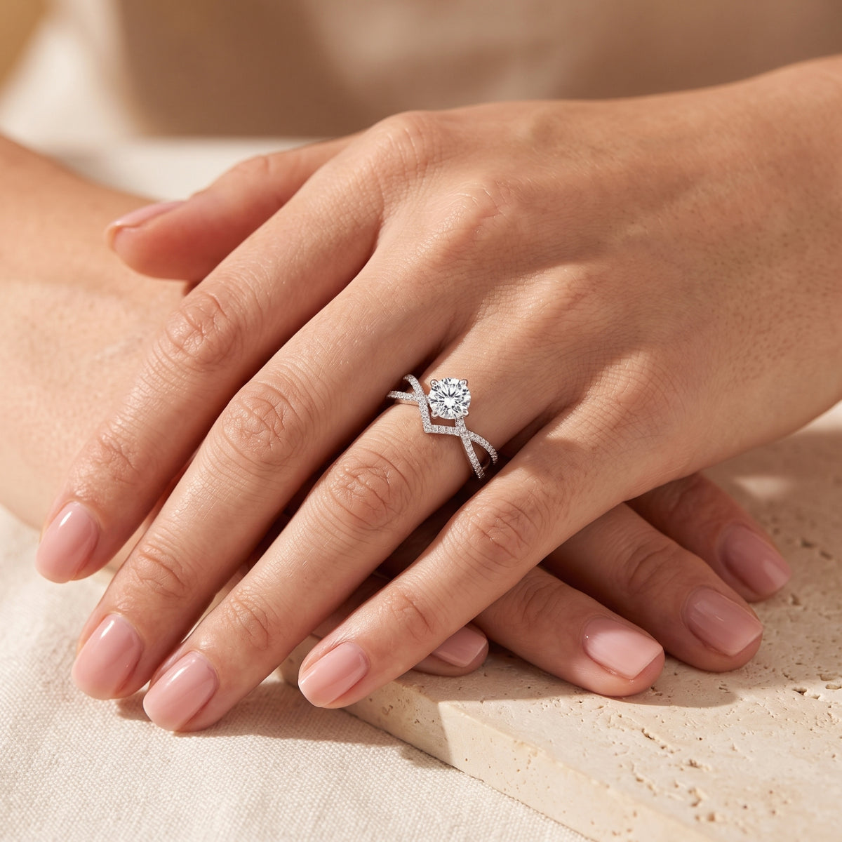 Pair of hands resting on a stone surface displaying the silver round solitaire ring on the ring finger.