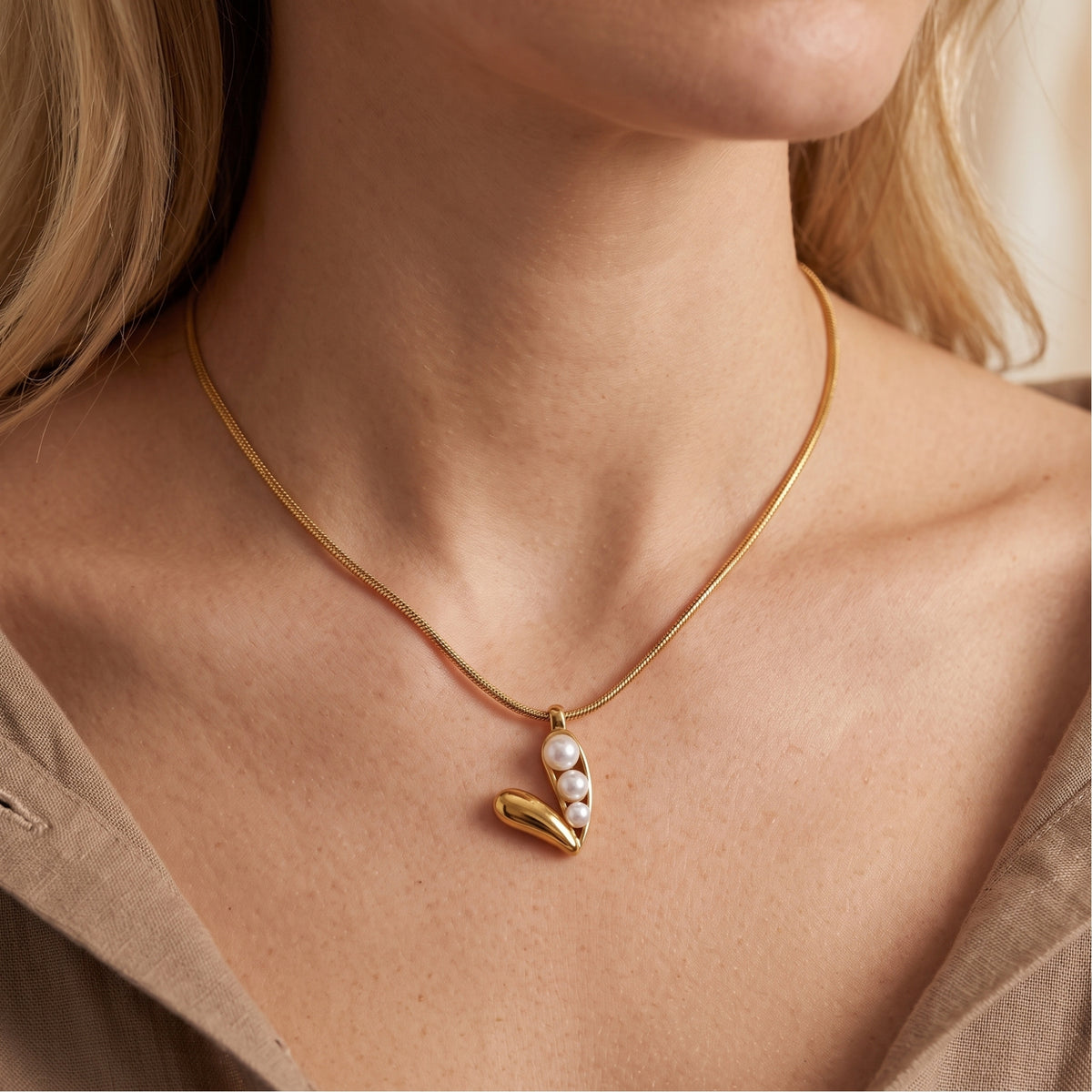 Frontal close-up of a model wearing the gold-tone three-pearl pod pendant necklace.