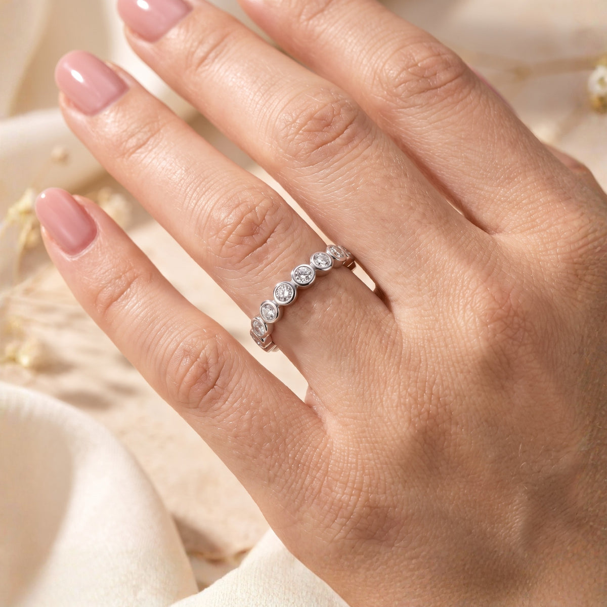 Angled top view of the silver bezel-set eternity band worn on a hand with nude manicured nails.