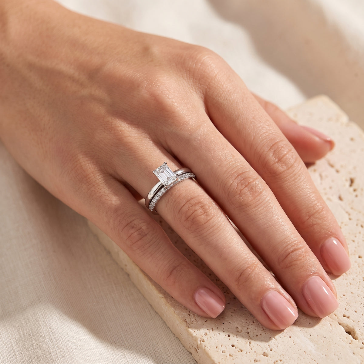 Hand wearing the silver emerald-cut ring and matching pavé band while resting on a stone block.