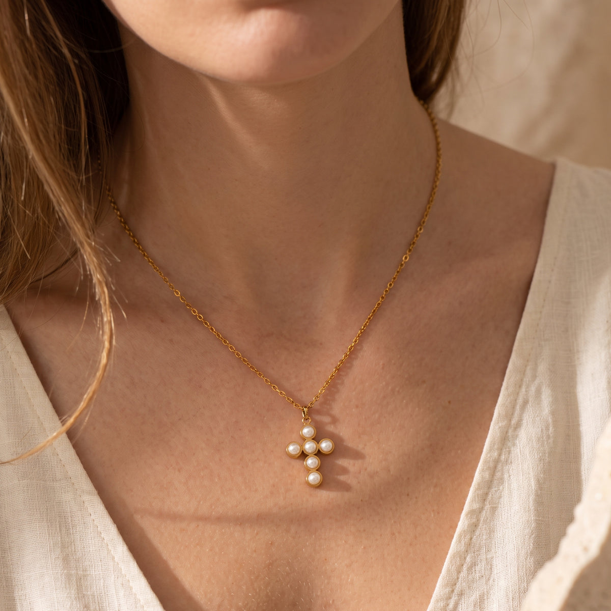 Model wearing the Elysian pearl cross necklace on a gold chain, styled with a cream V-neck top.