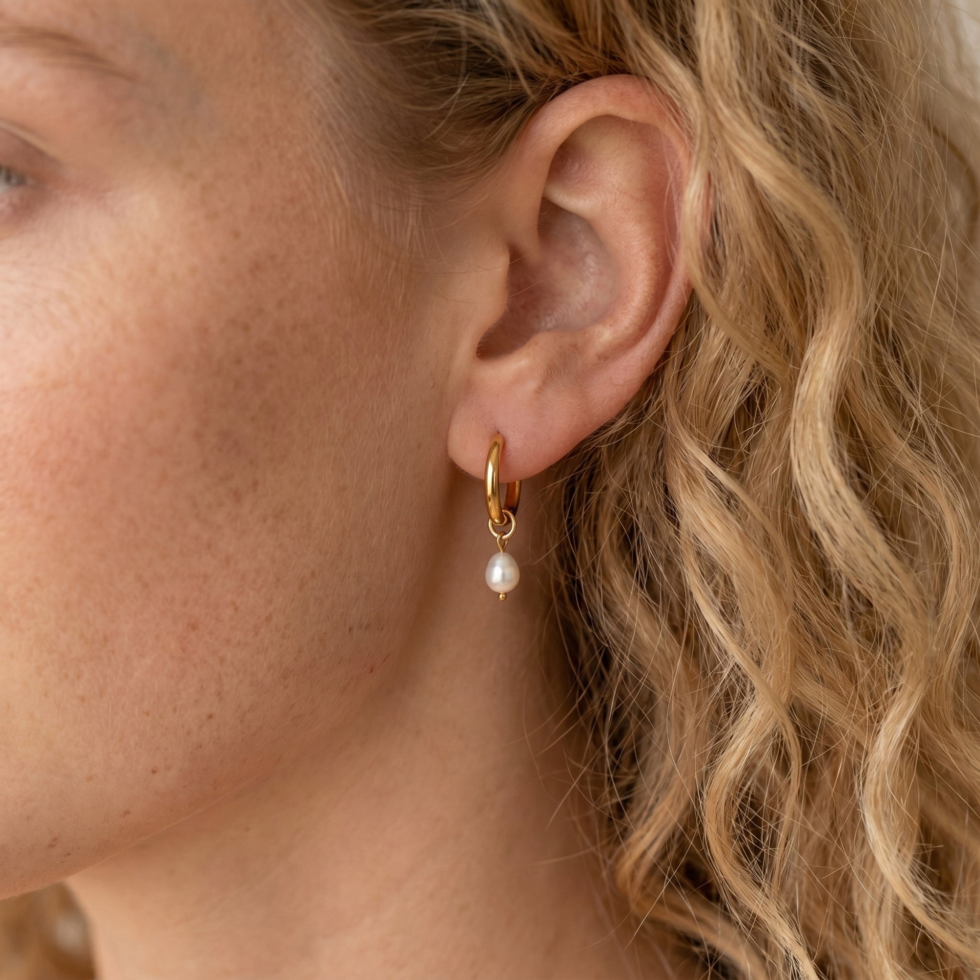 Model wearing a gold hoop earring with an oval pearl.