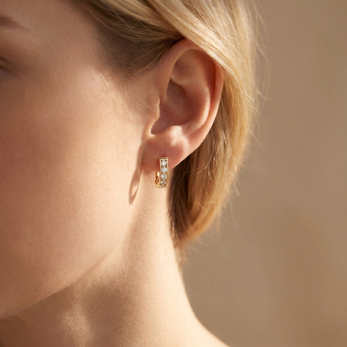 Gold hoop earring with round moissanite stones shown on a woman's ear.