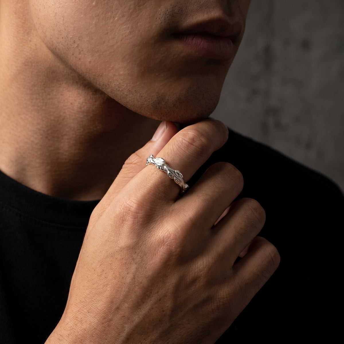 A man wearing the carved silver leaf band ring on his index finger in a low-key studio setting.
