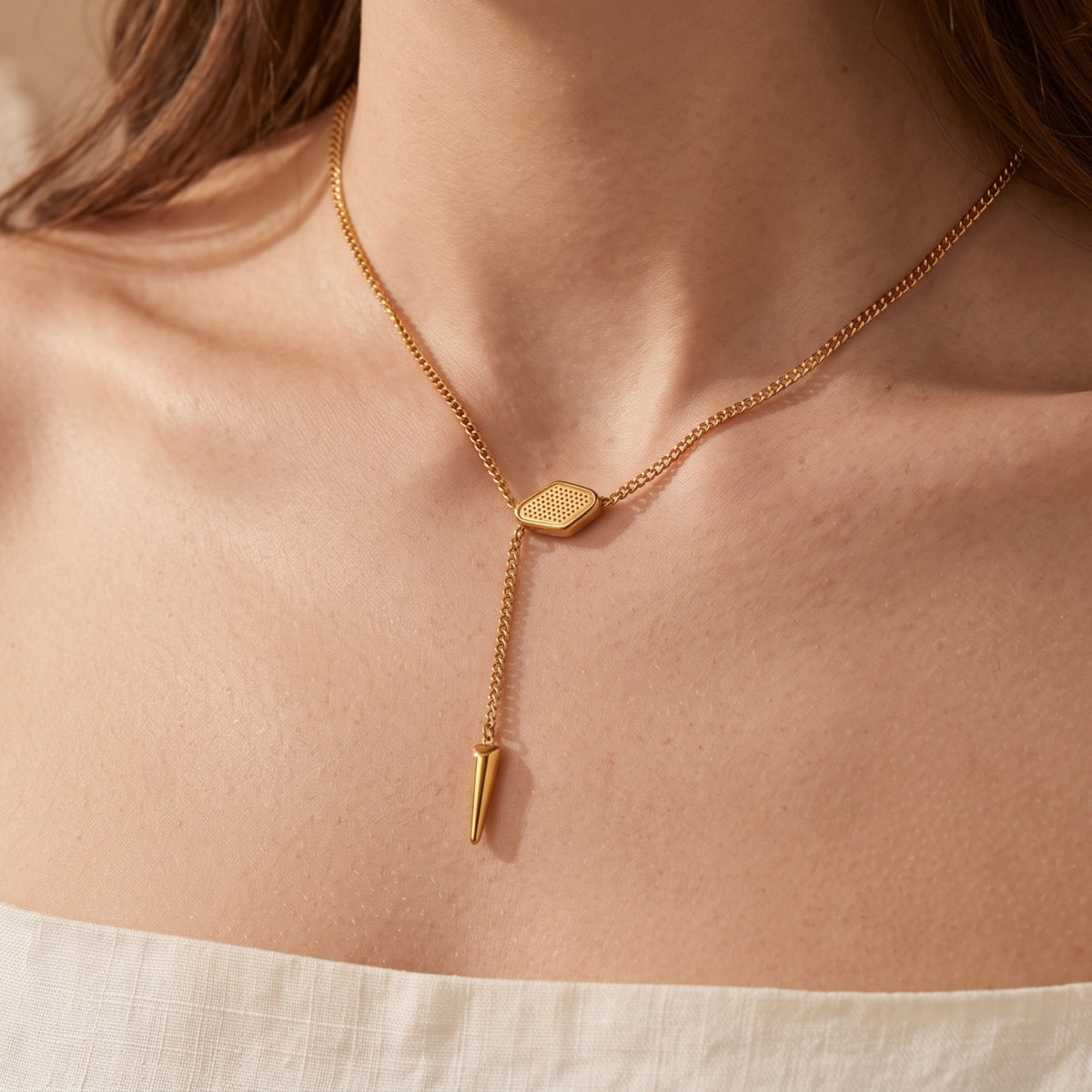 Gold lariat necklace with textured slider and spike pendant on a model's neckline.