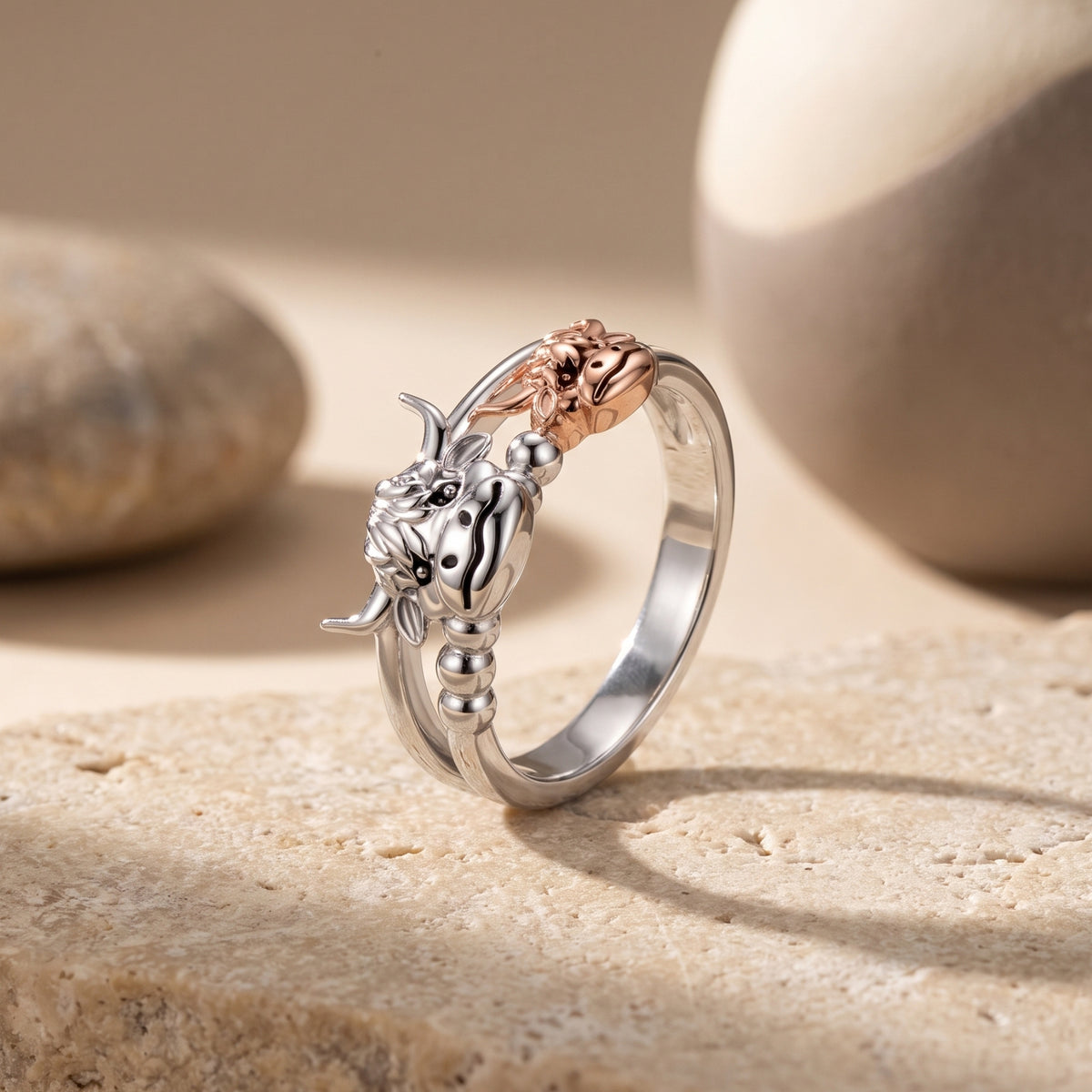 Angled view of a silver-tone highland cow ring with a rose gold-tone calf, standing on a stone surface.