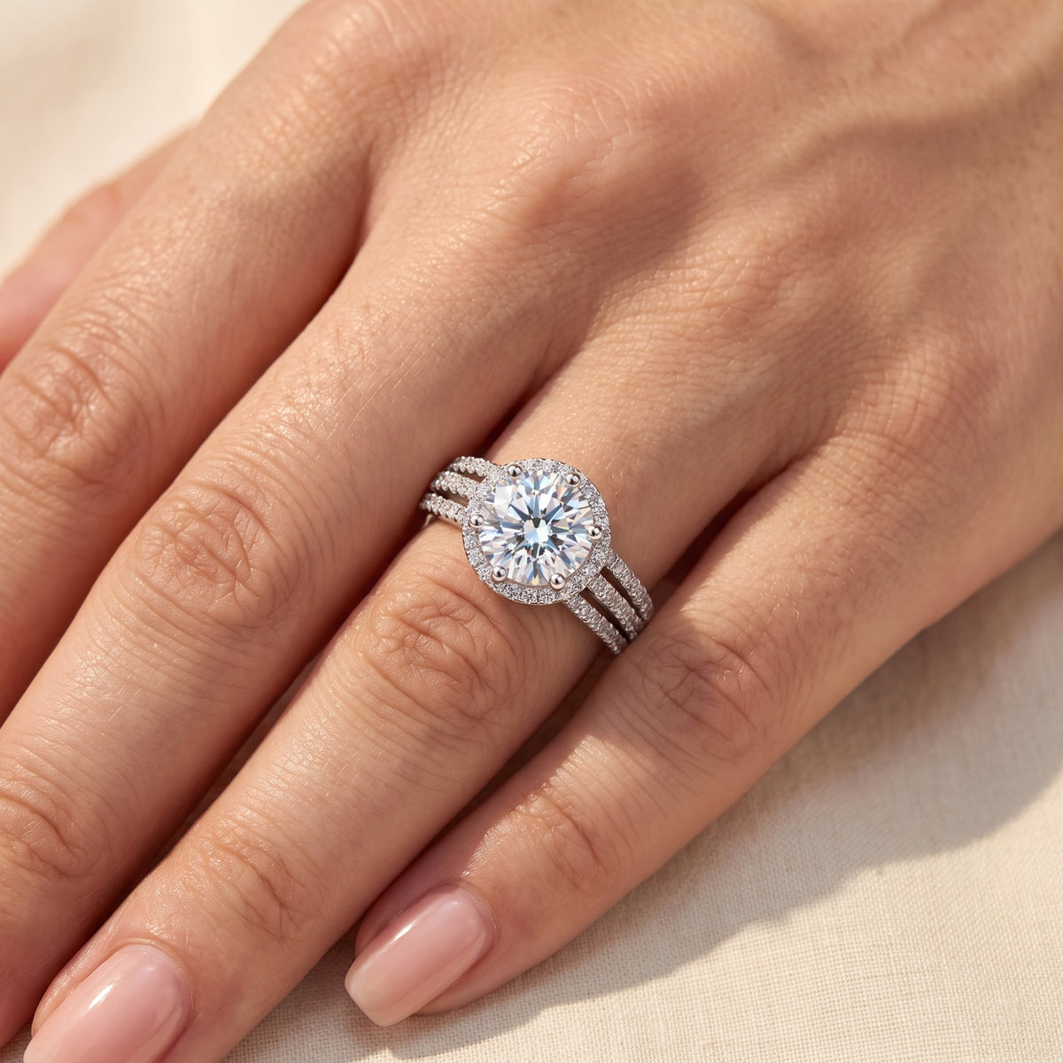 Close-up top view of the silver triple-band halo ring worn on a finger, showing the round stone and surrounding halo.