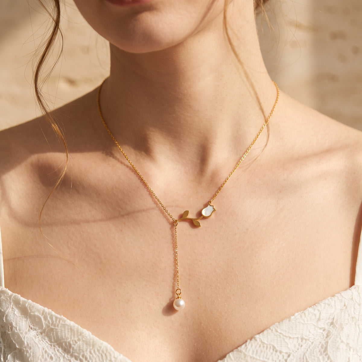 Model wearing the mother-of-pearl gold tulip lariat necklace with a pearl drop over a white lace neckline.