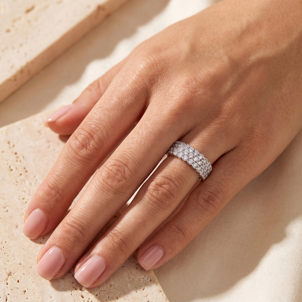 Overhead view of a hand wearing the silver scalloped triple-row clear-stone ring on the ring finger.