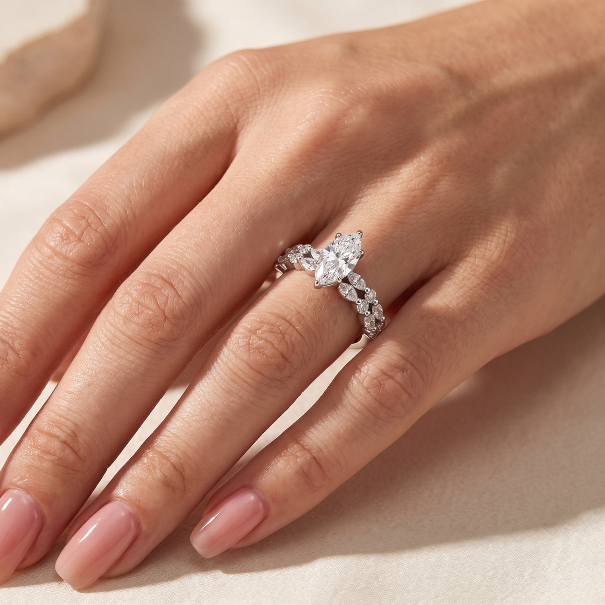 Silver marquise ring set worn on a hand in a wider view against a soft beige background.