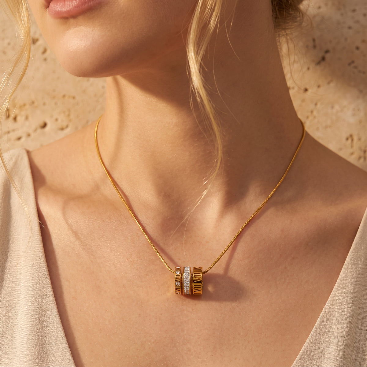 Front view of a gold-toned Roman numeral barrel pendant necklace worn on a model's chest.