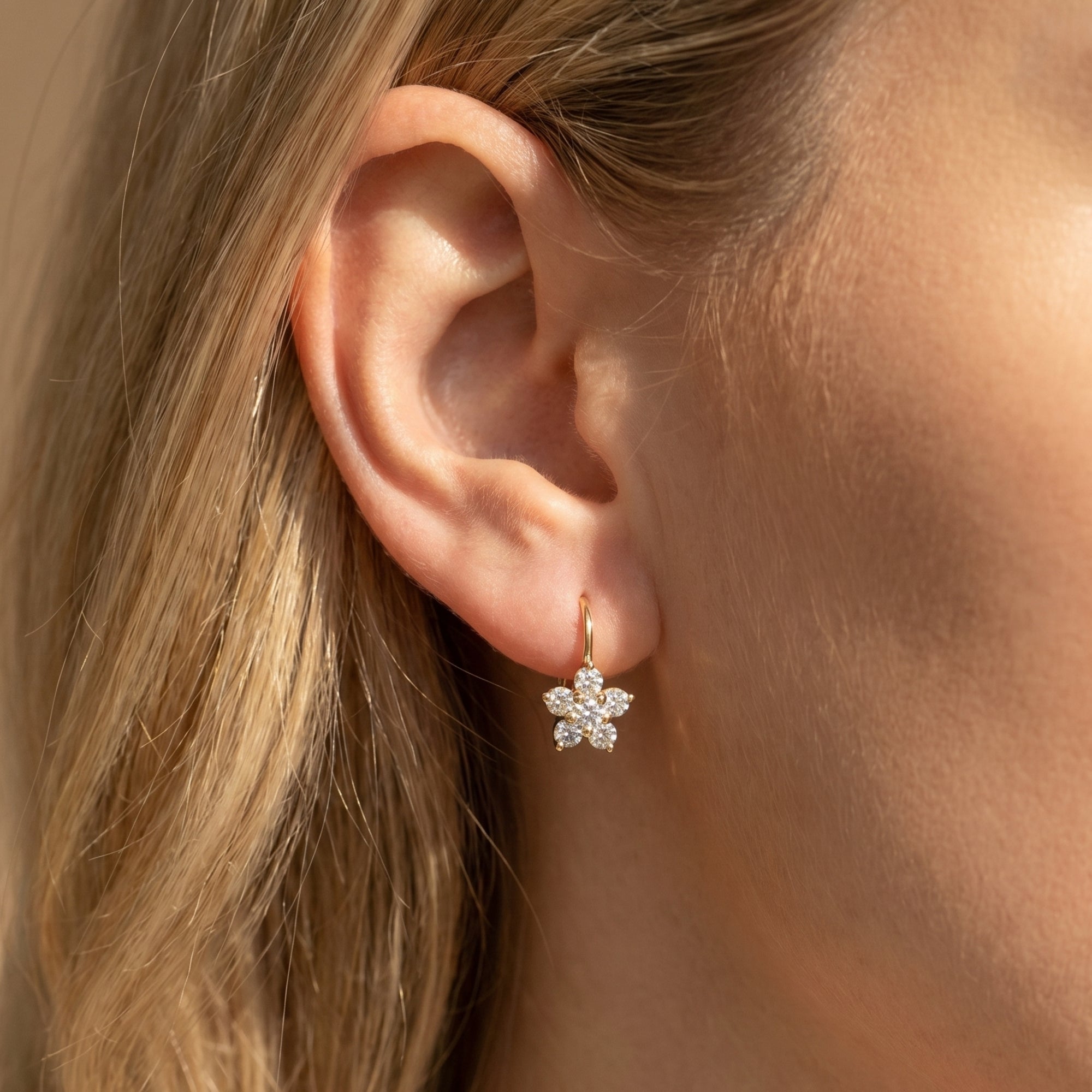 Gold floral drop earring with round moissanite stones worn on ear.