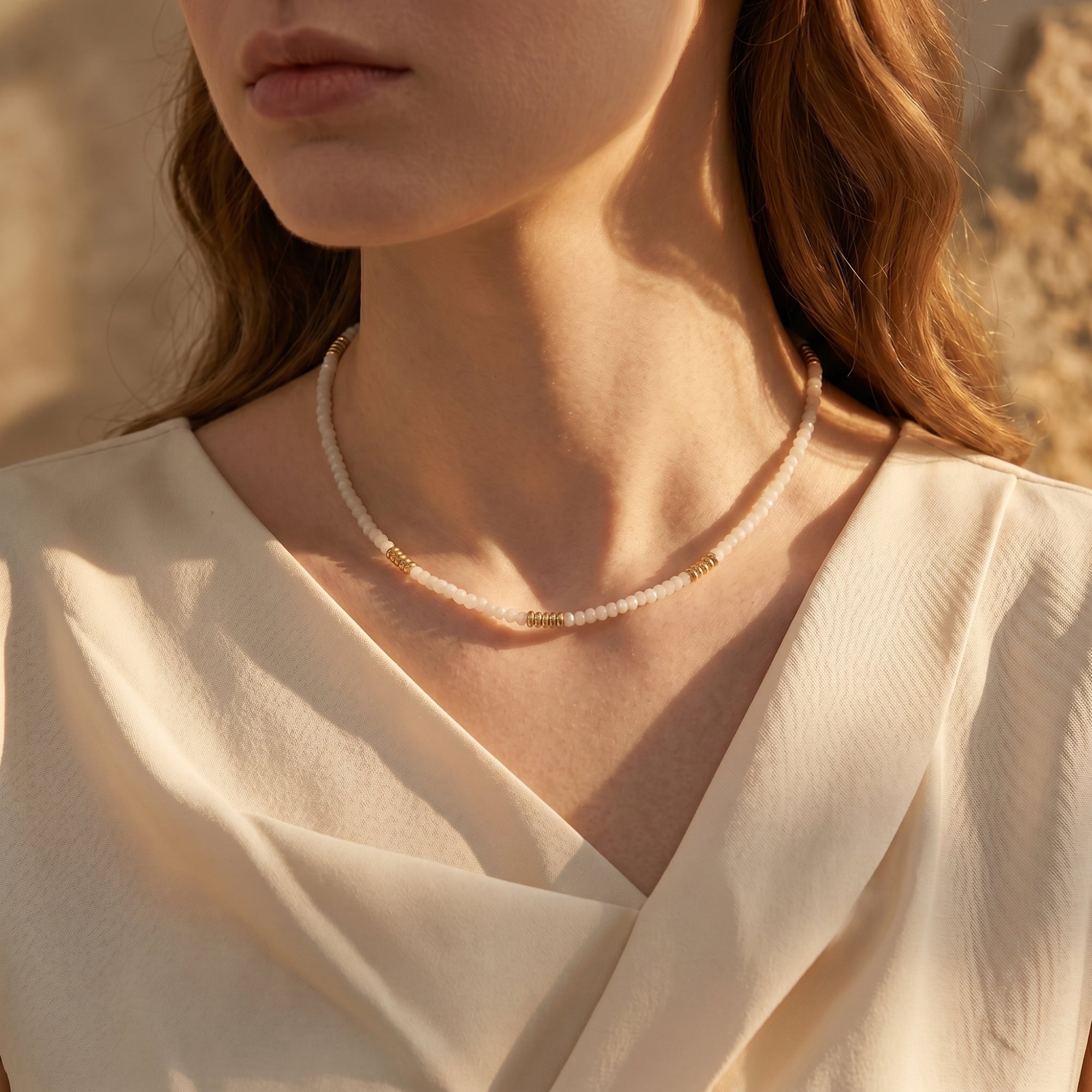 Woman wearing the Cassandra white quartz necklace with gold-tone beads and a cream blouse.