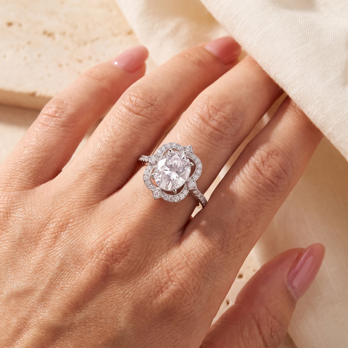 Top-down view of the silver ring with an oval center gem and scalloped halo worn on a hand.