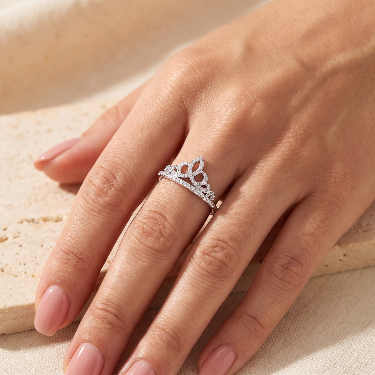 Silver tiara crown ring with cubic zirconia pave stones worn on a hand above a light stone surface.