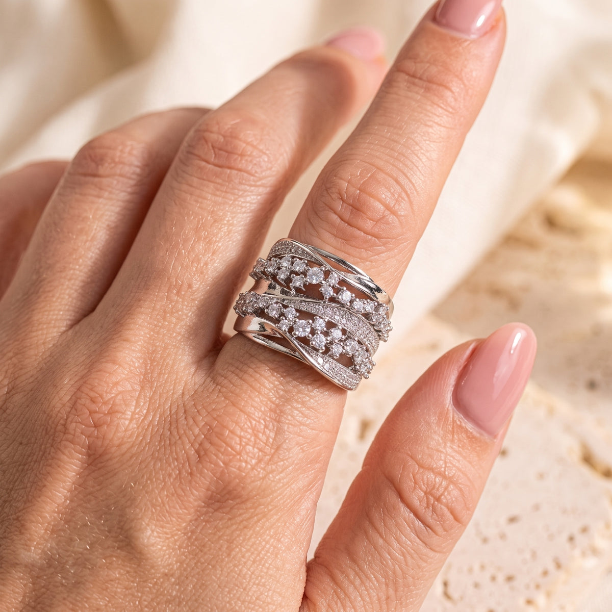 Close-up on a hand wearing the silver crossover ring, displaying its multi-row sparkling stone details.