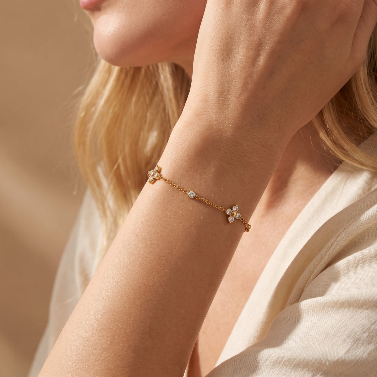 Close-up lifestyle view of the gold-tone station bracelet worn on a woman's wrist, showing clover and round stations.