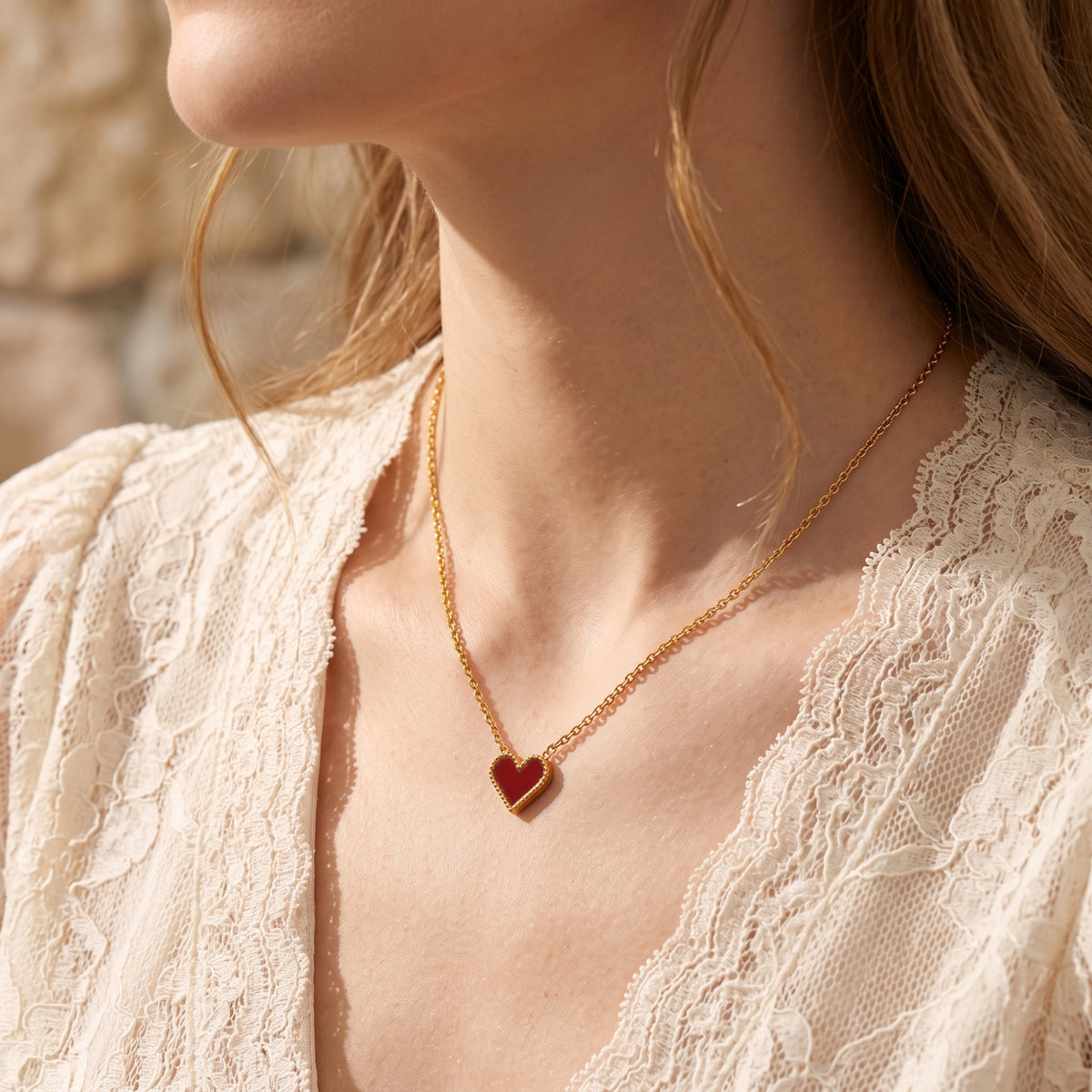 Model wearing the gold and scarlet heart necklace with a white lace top.