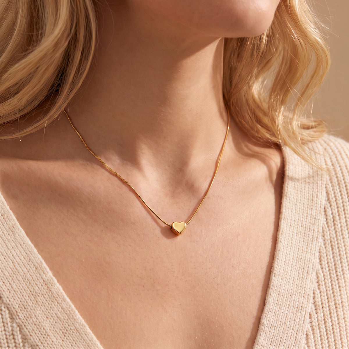 Front-facing view of a model wearing the gold-tone puffy heart pendant necklace over a cream knit cardigan.