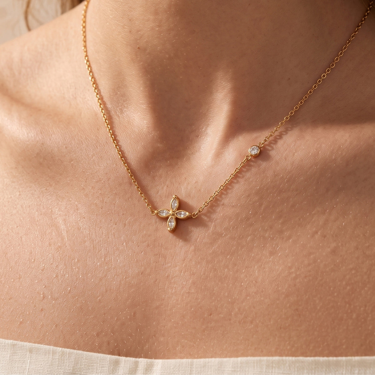 Close-up of the gold-tone four-petal flower necklace worn around a woman's neck.