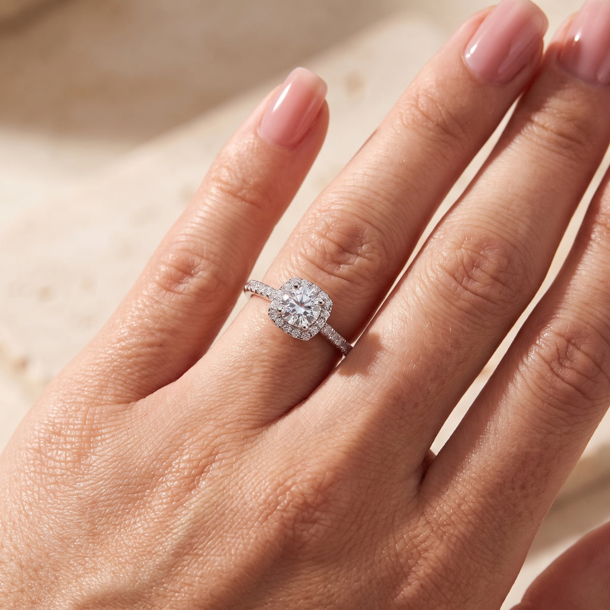 Close-up of the silver cushion halo ring worn on a hand angled toward the light.
