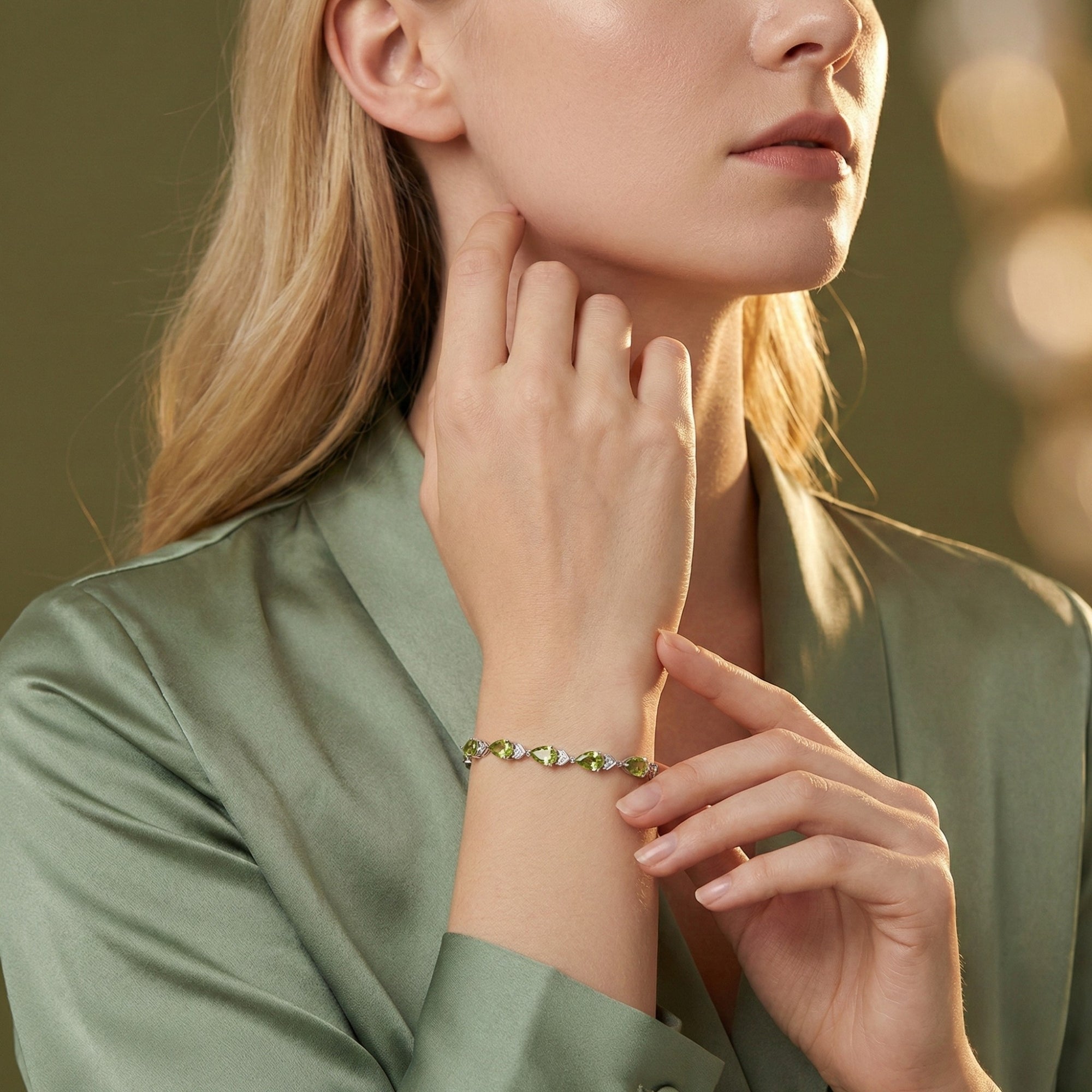 Woman wearing the sterling silver Quintina pear bracelet with green peridot stones, styled with a green silk top.