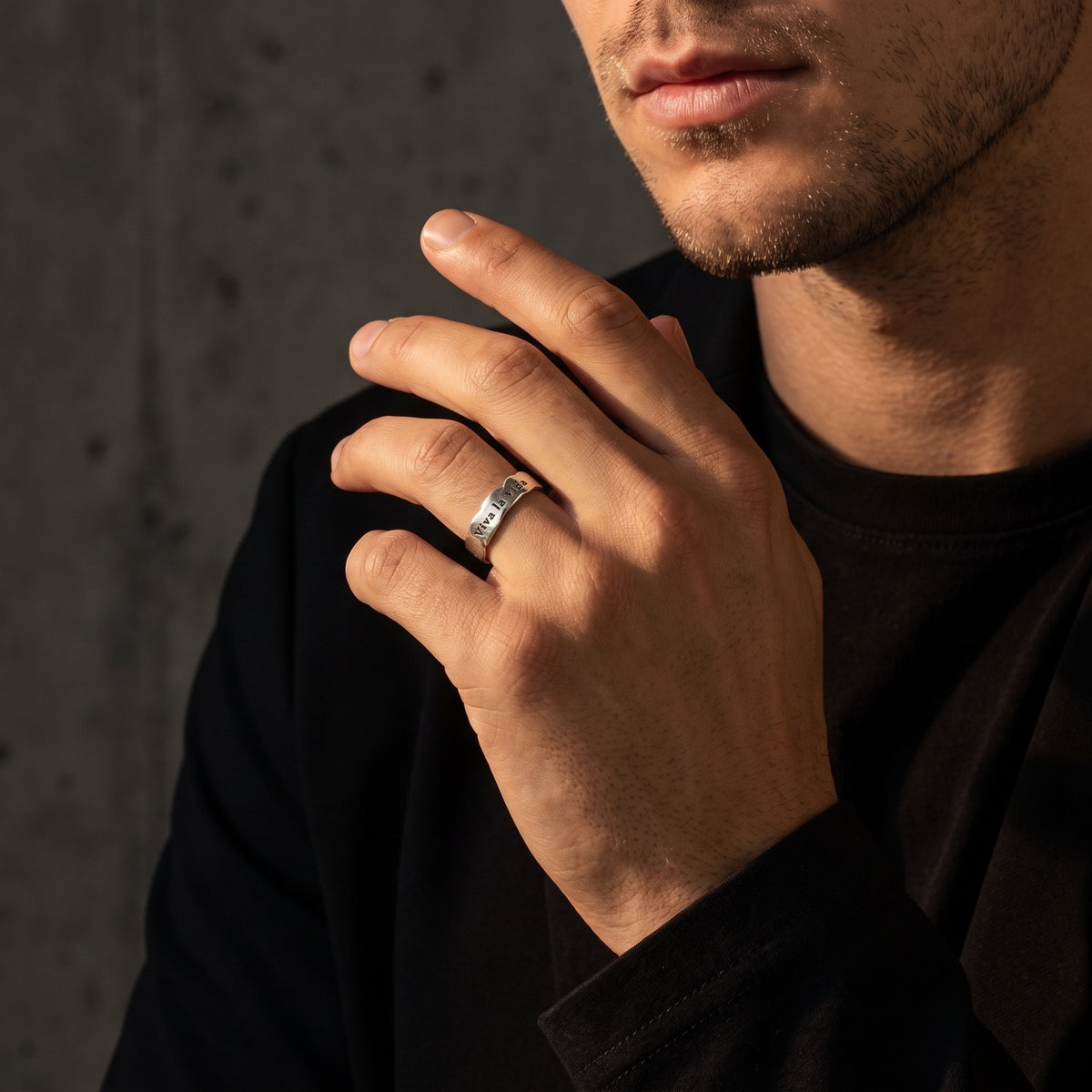 Wider model view of a man wearing the silver Viva la vida ring near his chest against a dark background.