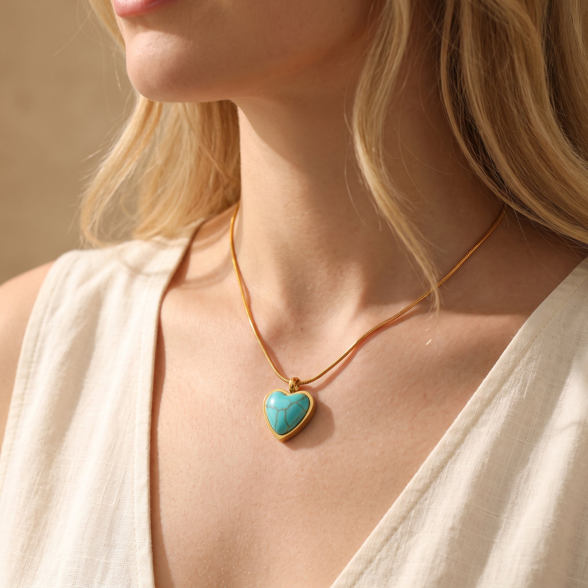 Model wearing the turquoise heart necklace on a gold-tone chain with a cream sleeveless top.