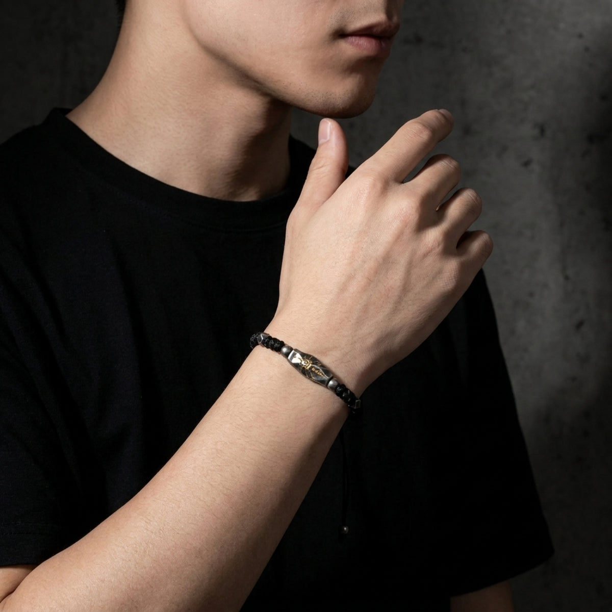 Sunburst rope bracelet worn on a wrist as the model raises his hand near his chin, showing the carved station and black cord.