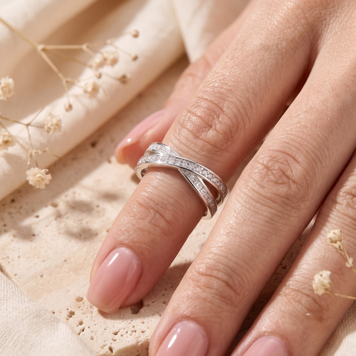 Angled view of the silver crossover ring with round simulated diamonds on a finger.