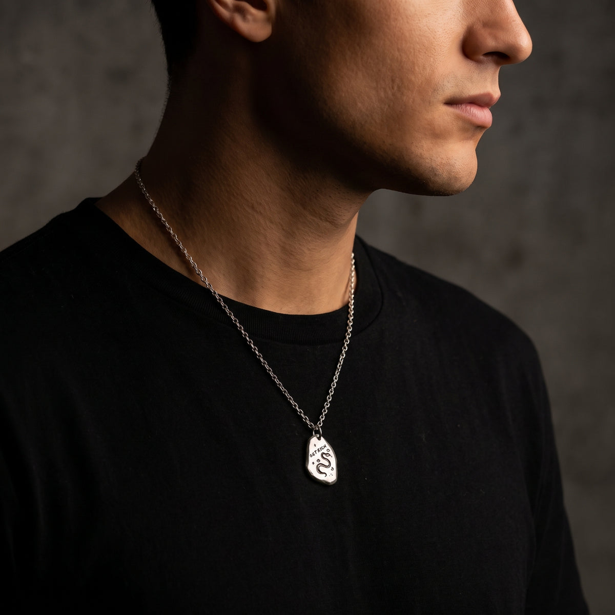 Three-quarter profile of a model wearing the silver snake pendant over a black shirt.