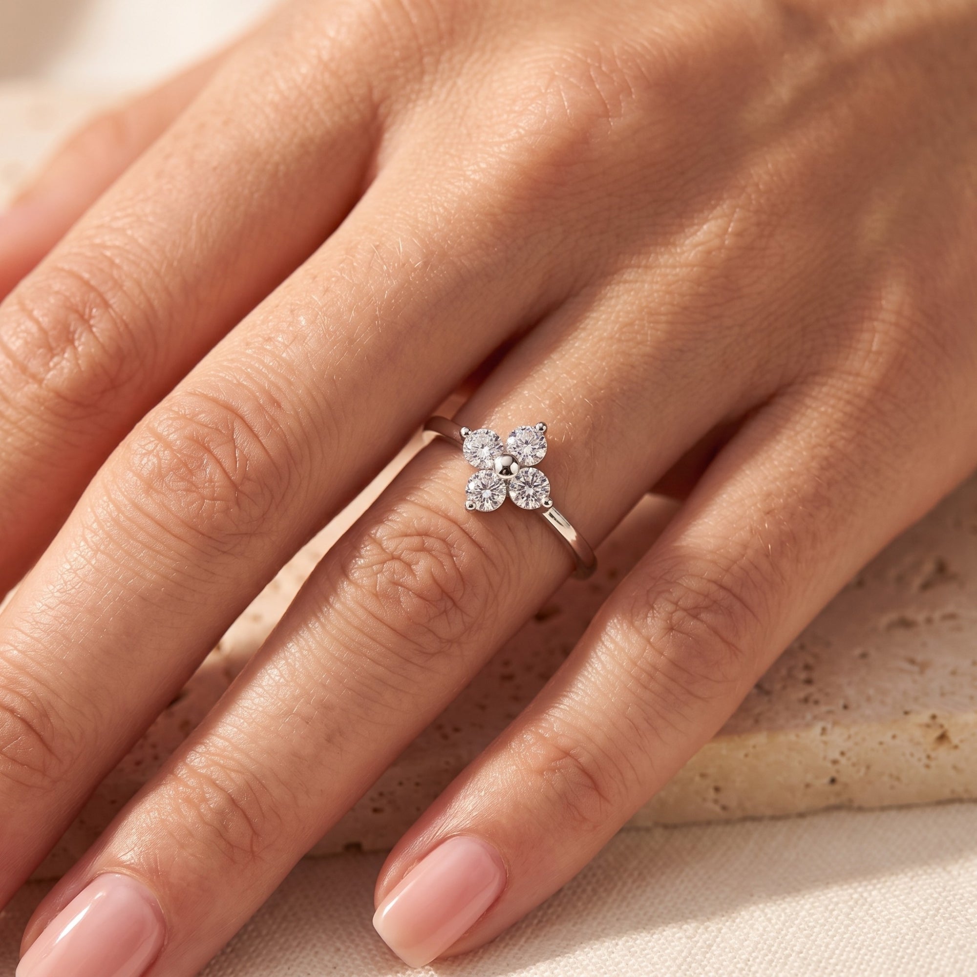 Silver clover promise ring with round simulated diamonds shown on a hand for scale.