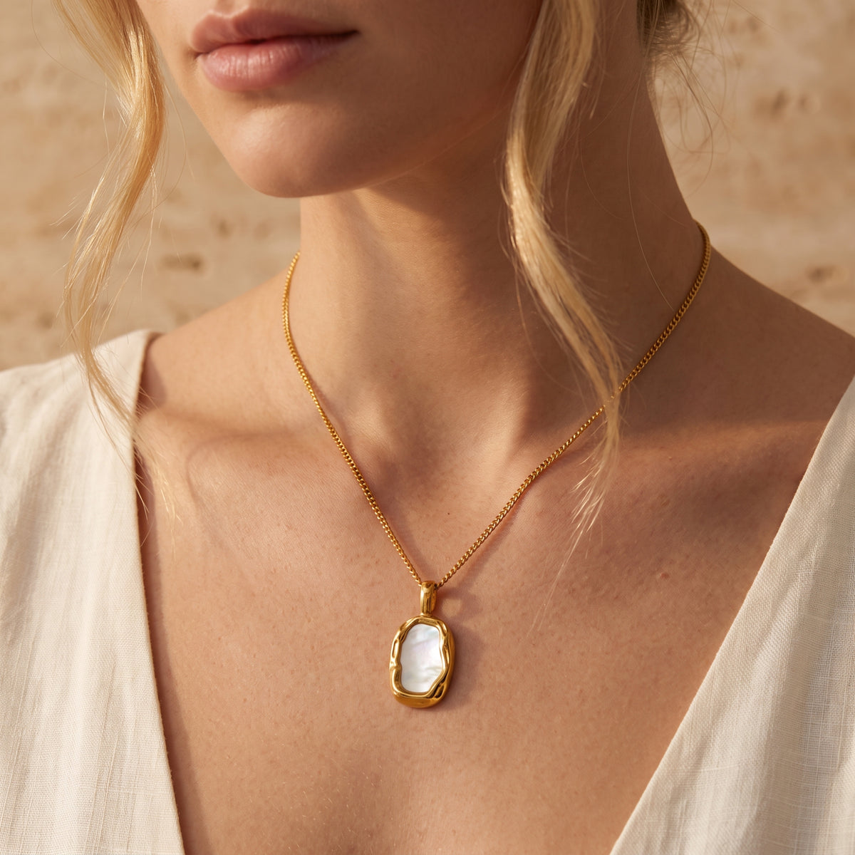 Front view of a model wearing the gold-tone shell pendant necklace with a cream V-neck top.