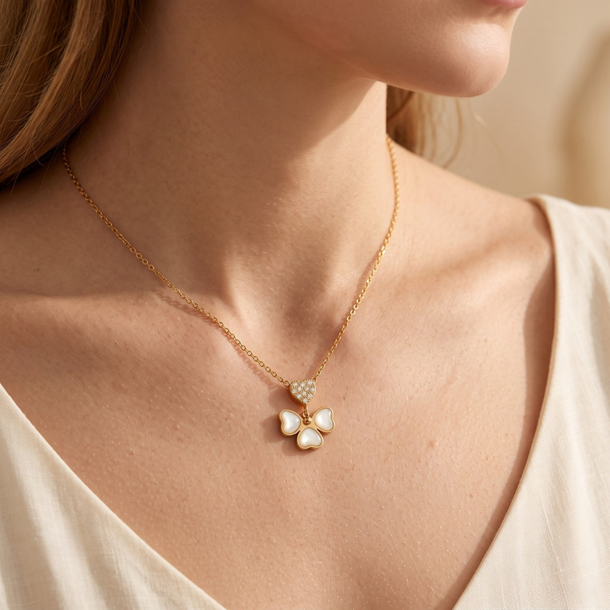 Wider model view of a gold-tone mother-of-pearl butterfly necklace with a pavé heart over a white V-neck top.